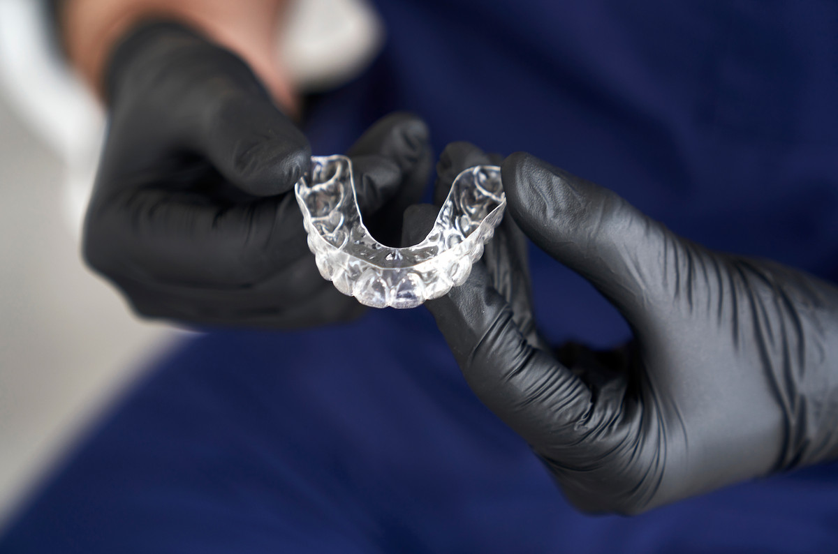 A TruAligner clear aligner held in a gloved hand
